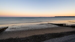 Ein Strand mit einer Holzpromenade, die zum Wasser führt, einem Kiesufer und einer entfernten Landmasse.