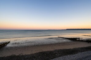 A beach with a wooden walkway leading to the water, a pebbly shore, and a distant landmass. - 5 Bed in Amroth (oc-pw9067) (Amroth)