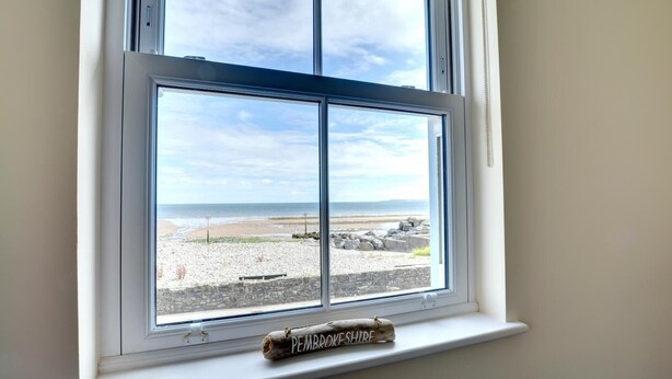 Ein Fenster mit freiem Blick auf einen Strand und die Küste von Pembrokeshire.