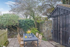 A rustic outdoor seating area with a table and chairs, surrounded by stone walls and greenery.