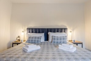 A neatly made bed with a patterned bedspread, two pillows, and two bedside tables with lamps and a coffee pot on one side.