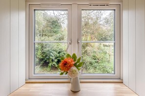 A room with a large window, a white vase with flowers, and a wooden floor. - 2 Bed in Moylegrove (oc-f33508) (Cardigan)