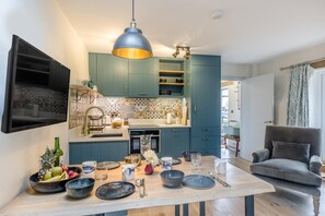 Une cuisine moderne avec des meubles de couleur turquoise, une table à manger en bois dressée avec de la vaisselle, et un luminaire suspendu.