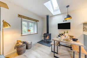 A cozy room with a wood-burning stove, a dining table, wicker baskets, and a window with a view.