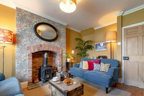A cozy living room with a brick fireplace, a blue sofa with cushions, a coffee table with a book and a teapot, and a large mirror on the wall. - 2 Bed in Pickering (oc-y110) (Pickering)