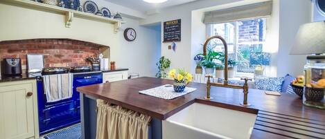 A kitchen with a blue stove, a sink, and a window with a view of the outside. There is a clock on the wall and a sign with notices.