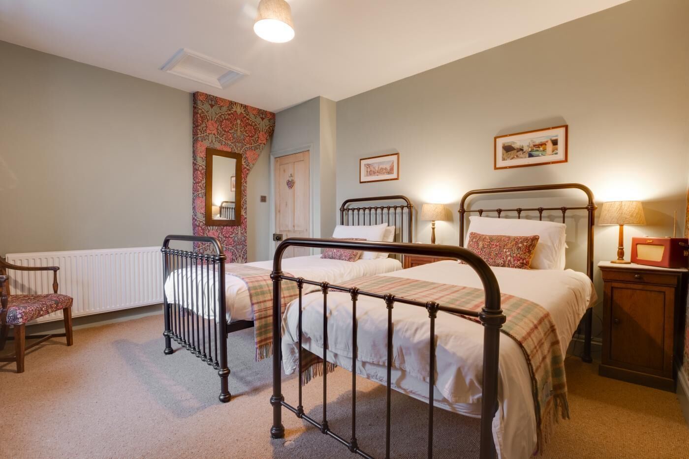 Een slaapkamer met twee bedden, een stoel, een radiator en een nachtkastje met een lamp.