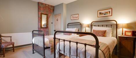 A bedroom with two beds, a chair, a radiator, and a bedside table with a lamp.