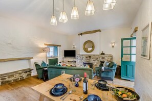 A cozy living room with a stone fireplace, green sofas, a wooden dining table set for four, and a television. - 2 Bed in Moylegrove (oc-g33509) (Cardigan)