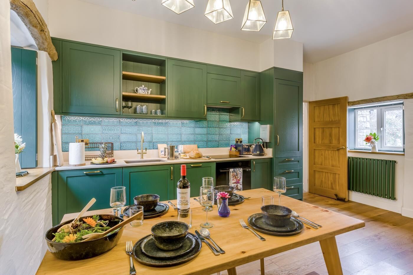 Una cocina con armarios verdes, una mesa de madera lista para comer y una ventana con vistas.