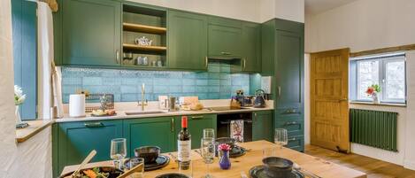 Una cocina con armarios verdes, una mesa de madera lista para comer y una ventana con vistas.