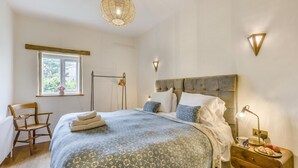 Ein Schlafzimmer mit Bett, Nachttisch, Lampe, Stuhl, Fenster und einer Pendelleuchte.