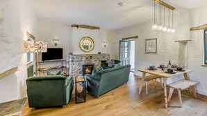 Ein Wohnzimmer mit Kamin aus Stein, grünen Sofas, einem Holzesstisch und einem Fernseher.