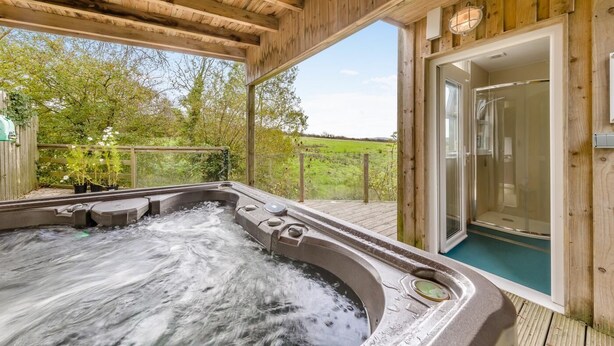 Eine Holzterrasse mit Whirlpool und einer gläsernen Duschkabine.