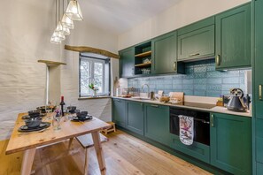 A kitchen with green cabinets, a wooden table set for dining, and a window with a view. - 2 Bed in Moylegrove (oc-g33509) (Cardigan)