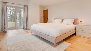 A bedroom with a large bed, a nightstand, a wooden floor, and a view through a glass door. - 4 Bed in Rock (oc-nb1952) (Rock)