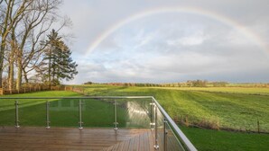 A wooden deck with a glass railing overlooking a grassy field and a rainbow in the sky. - 4 Bed in Rock (oc-nb1952) (Rock)