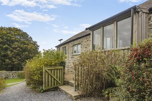 A stone building with a wooden gate, a gravel path, and various shrubs and trees. - 2 Bed in Moylegrove (oc-s33510) (Cardigan)