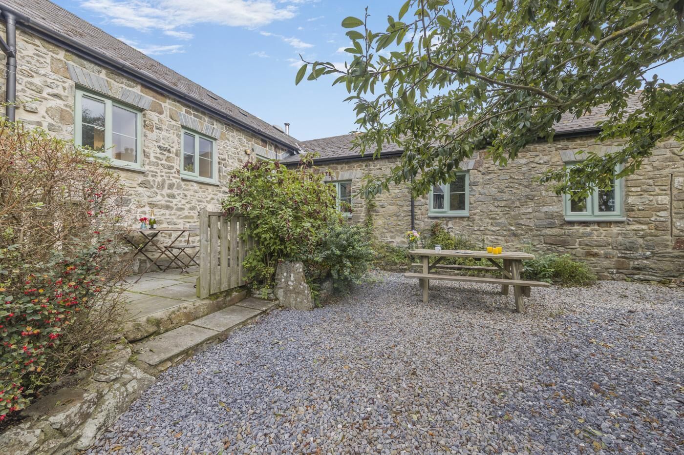 A stone building with a gravel courtyard, a wooden table, and a chair.
