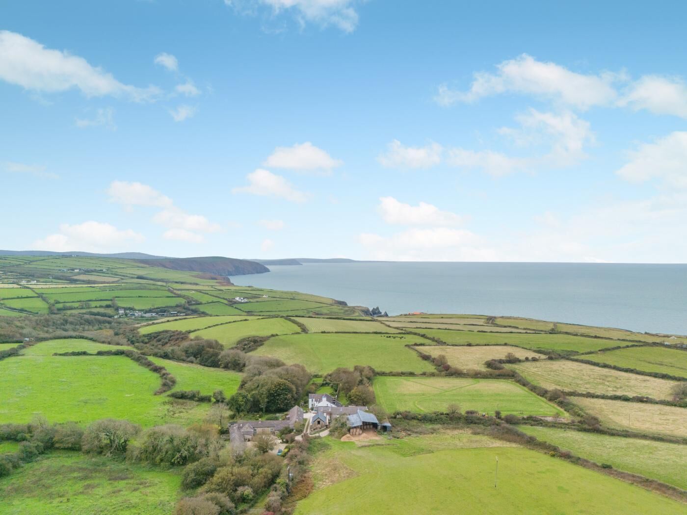 A rural landscape with fields, a house, and a coastline.