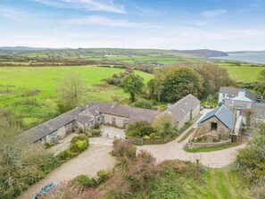 A rural property with stone buildings, a gravel driveway, and a view of the surrounding countryside and water body. - 1 Bed in Moylegrove (oc-l33511) (Cardigan)