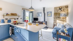 A modern kitchen with blue cabinets, a central island, and a dining area with a blue sofa and a fireplace.