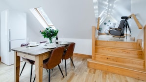 Ein moderner Essbereich mit einem Holztisch, gedeckt für vier Personen, einer Blumenvase und einer Weinflasche. Im Hintergrund ist eine Treppe mit einer Kamera auf einem Stativ zu sehen.