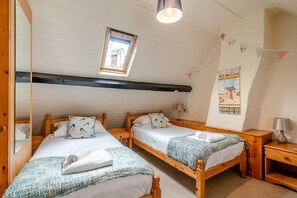 Een kamer met twee houten bedden, een dakraam, een wandplank met een afbeelding en een klein tafeltje met een lamp.