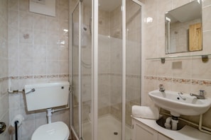 Een badkamer met toilet, douchecabine, wastafel en spiegel.