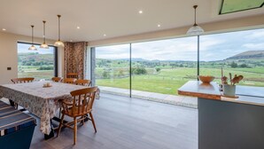 Un coin repas avec une table dressée pour six personnes, de grandes fenêtres donnant sur un paysage verdoyant et un éclairage suspendu.