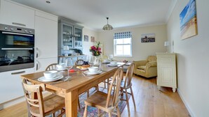 A modern kitchen with built-in appliances, a dining area with wooden furniture, and a cozy living space with a sofa and a cabinet. - 5 Bed in Amroth (oc-pw9068) (Amroth)