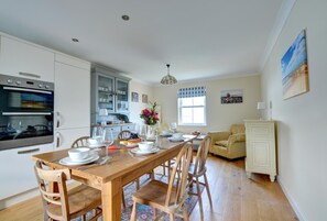Eine moderne Küche mit eingebauten Geräten, ein Essbereich mit Holzmöbeln und ein gemütlicher Wohnbereich mit Sofa und Schrank.