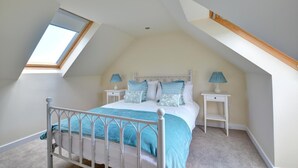 A bedroom with a sloped ceiling, a skylight, a bed with a white metal frame, two bedside tables with lamps, and a carpeted floor. - 5 Bed in Amroth (oc-pw9068) (Amroth)
