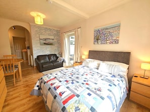 A bedroom with a bed, a desk, a chair, a sofa, a window with curtains, and a painting on the wall.