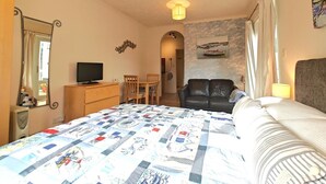Une chambre à coucher avec un lit, un bureau avec une télévision, une chaise, un canapé et un tableau accroché au mur.