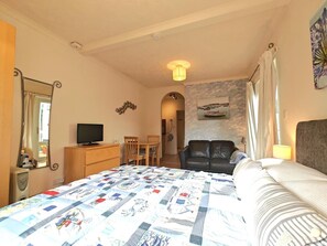 A bedroom with a bed, a desk with a TV, a chair, a couch, and a painting on the wall. - 1 Bed in Lyme Regis (oc-a33559) (Lyme Regis)