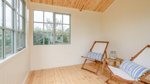Ein Zimmer mit großen Fenstern, Holzboden und zwei Holzstühlen mit gestreifter Polsterung.
