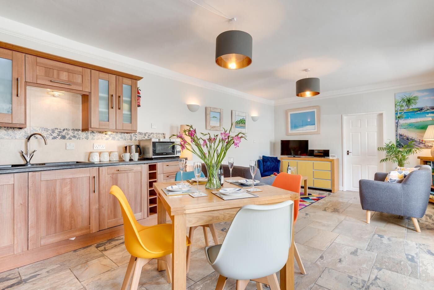 A modern kitchen with wooden cabinets, a dining table with chairs, and pendant lighting.