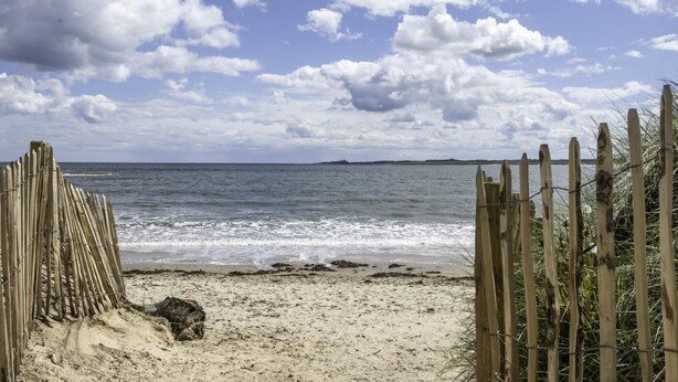 Ein Strand mit einer Holzumzäunung und einem sandigen Pfad zum Wasser.