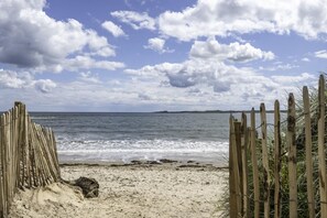Una playa con una valla de madera y un sendero arenoso que conduce al agua.