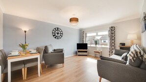 Ein modernes Wohnzimmer mit Esstisch, zwei Sofas, einem Fernseher und einem großen Fenster mit Vorhängen.