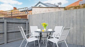 Eine Terrasse mit Tisch und vier Stühlen, einem Blumenvasen und einem Holzzaun.