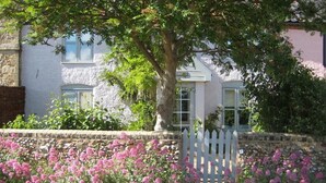A stone wall with a white picket fence and pink flowers in front of a building with a window and a door. - 2 Bed in Snape (oc-sfbox) (Snape)
