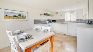 A modern kitchen with white cabinets, a dining table set with white plates and bowls, and a tiled backsplash. - 2 Bed in Snape (oc-sfbox) (Snape)
