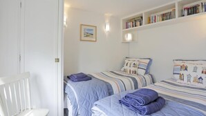 A bedroom with two beds, a white chair, a bookshelf, and a framed picture on the wall. - 2 Bed in Snape (oc-sfbox) (Snape)