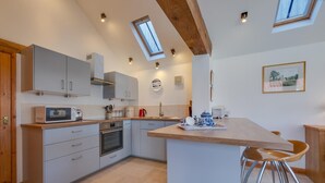 Une cuisine moderne dotée d’un îlot central, d’appareils électroménagers intégrés et d’un plafond en pente agrémenté de lucarnes.