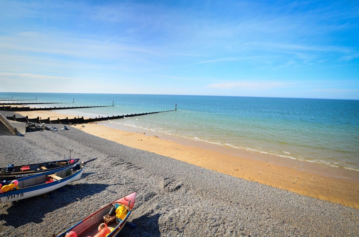 A beach with a pebble shore, a pier extending into the sea, and two boats on the sand.