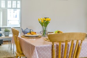 A dining table with a polka dot tablecloth, a vase with yellow flowers, a teapot, and waffles with berries.