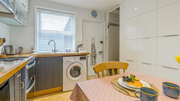 A compact kitchen with a washing machine, a dining table with a polka dot tablecloth, and a chair. - 2 Bed in Holt (oc-2231) (Holt)