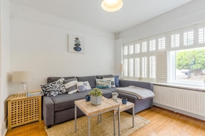 A living room with a grey sofa, a wooden coffee table, and a window with shutters.